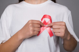 World Breast Cancer Day Concept. Health care woman wore white t-shirt with red ribbon for awareness. Symbolic bow color raising on people living with women’s breast tumor illness